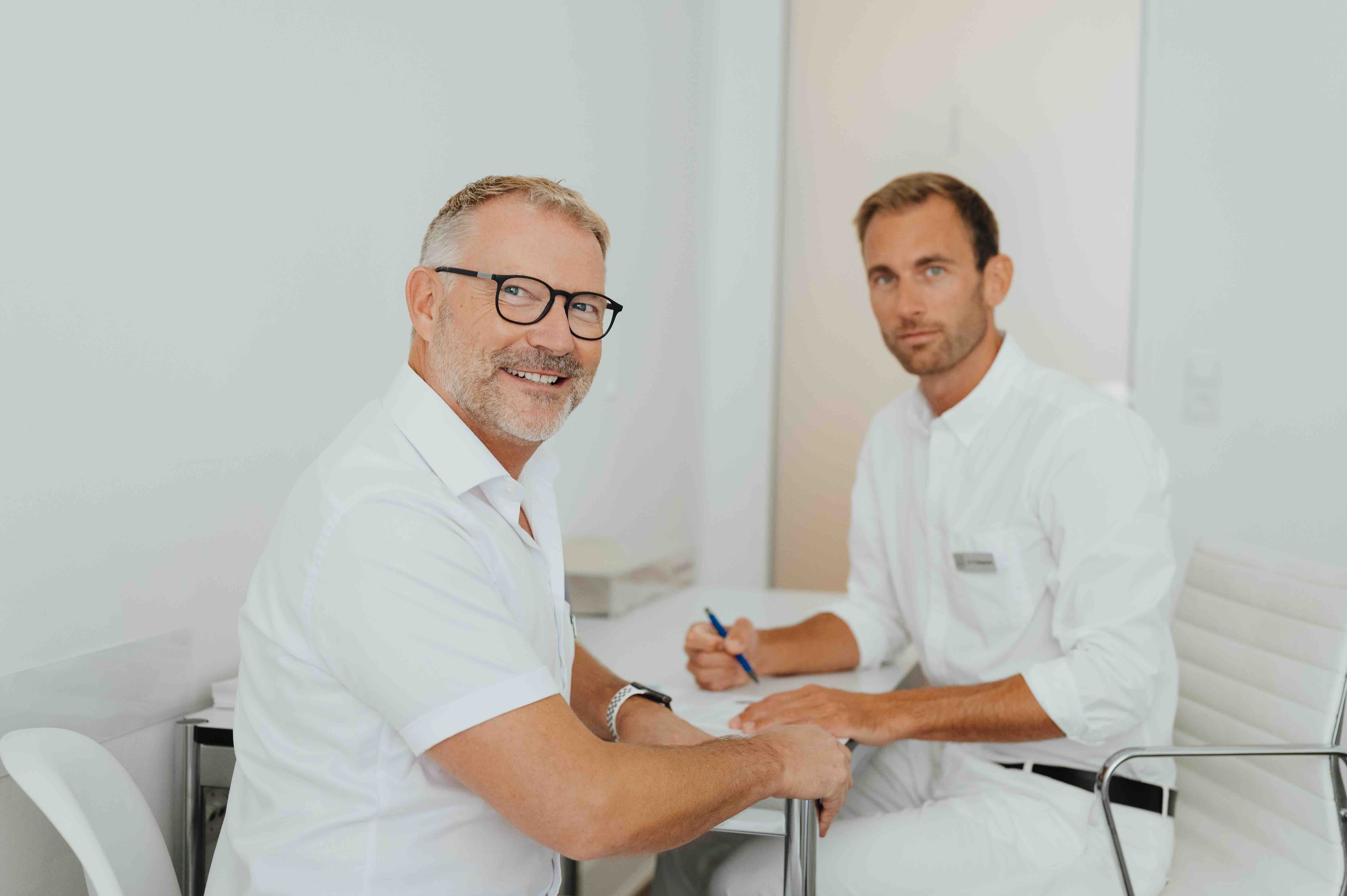 Dr. Bergmann und Dr. Kruess sitzen am Tisch und besprechen gemeinsam eine Patientenbehandlung.